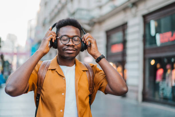 joven alegre escuchando música mientras camina por la calle. - financial district audio fotografías e imágenes de stock