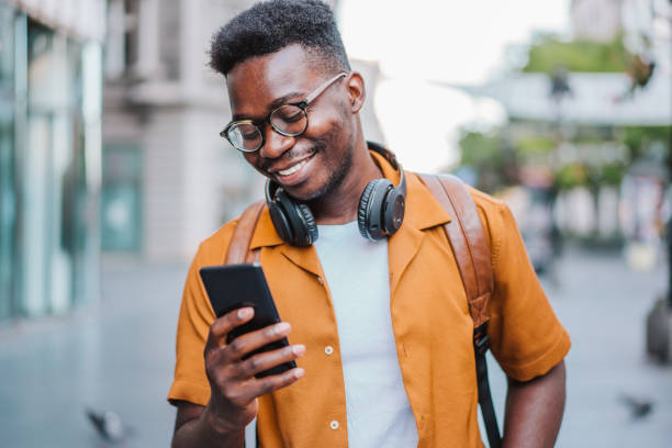 istock Cheerful young man using smartphone while walking on the street. 1387051534