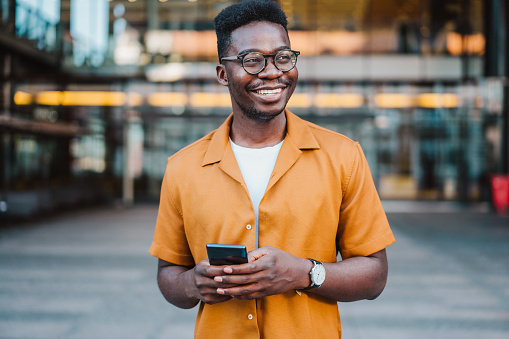 Young smiling man using smartphone on the street.
