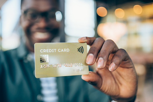 Shot of handsome young male shopper holding a credit card - focus on foreground. Man showing gold colored credit card against the camera. Focus is on the card.