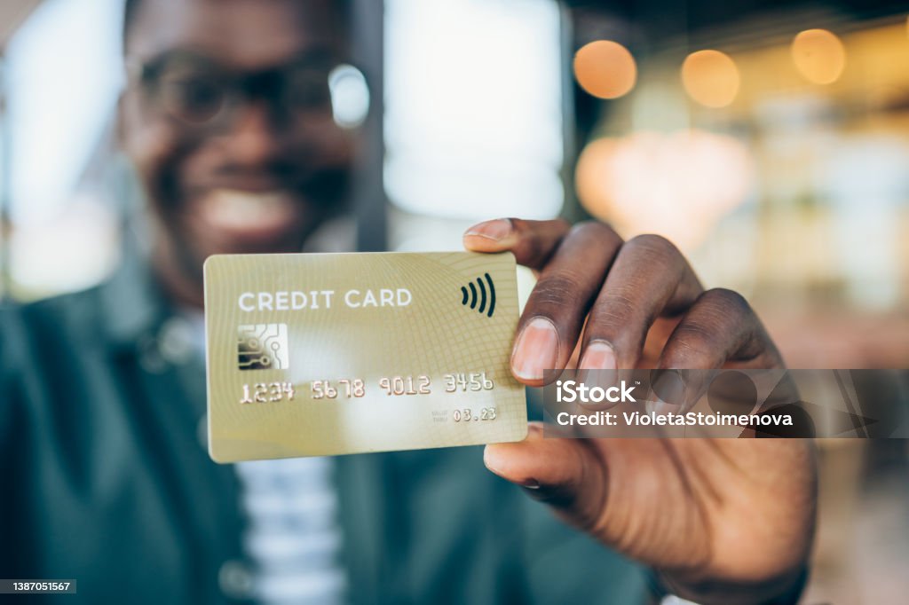 Man holding a credit card. Shot of handsome young male shopper holding a credit card - focus on foreground. Man showing gold colored credit card against the camera. Focus is on the card. Credit Card Stock Photo