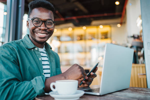 istock Young man sitting in coffee shop using laptop and smartphone. 1387051570