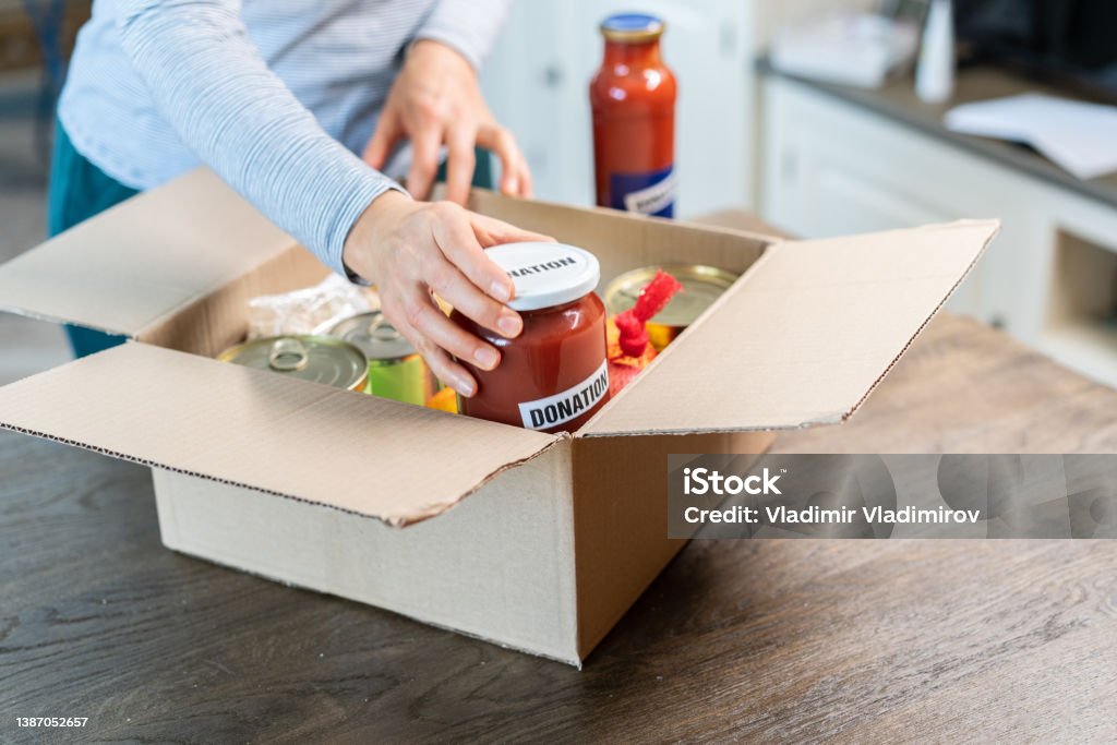Unrecognisable person is filling a box with food to donate people in need Unrecognisable person is filling a box with food to donate people in need, closing the box and glueing a table "Donation" Ukraine Stock Photo