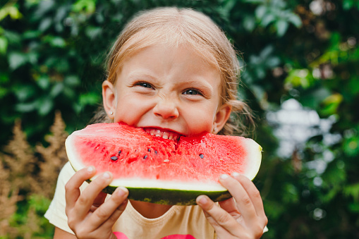 Happy funny child girl eats watermelon outdoor. Summertime