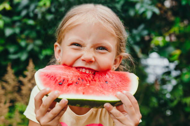Happy funny child girl eats watermelon outdoor stock photo