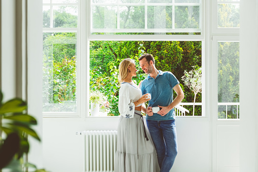 Smiling mid adult couple having coffee together near window in apartment.