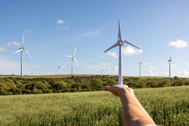 istock Engineer in the fields holding a wind turbine model with real ones on background 1387054769