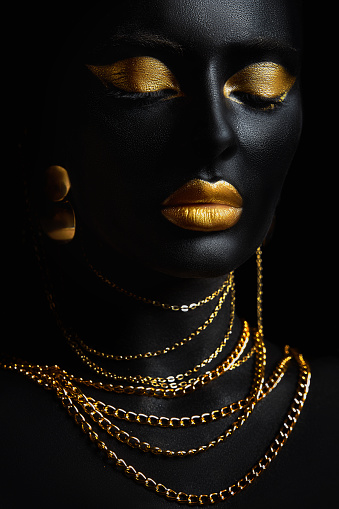 Beauty gold makeup lips eyelids woman black skin color body art, gold jewelry chain, fingertips nails in gold color paint. Professional gold makeup