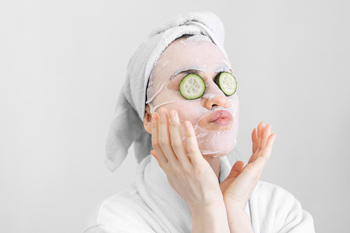 Young woman with a sheet mask on her face, spa procedure, moisturizing and nourishing facial skin.