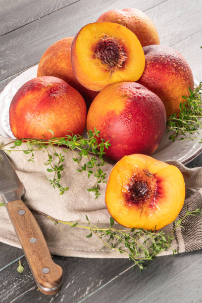 ripe peaches with thyme leaves in a plate on a wooden board on a background - nectarine imagens e fotografias de stock