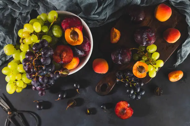 Freshly washed fruits with water droplets. bright high key look conveys freshness. Variety of fresh grapes, apricot and plumes on dark background. Fruit sources of vitamins