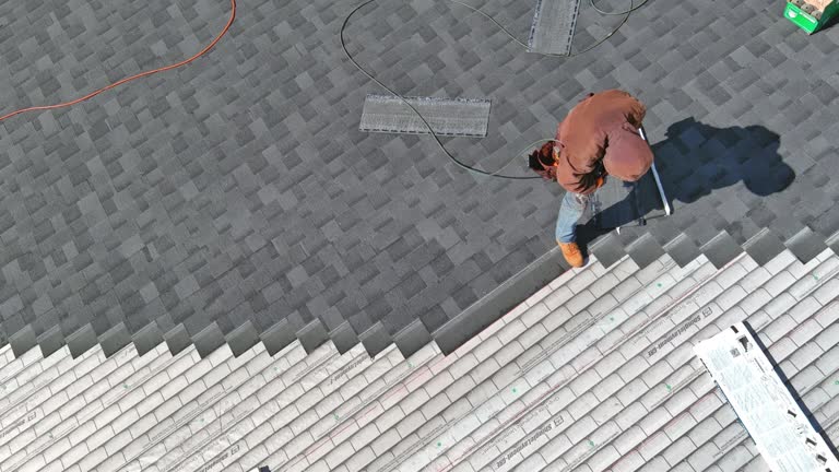 A asphalt shingles installation on the roof roofer is nailing asphalt shingles to roofing construction