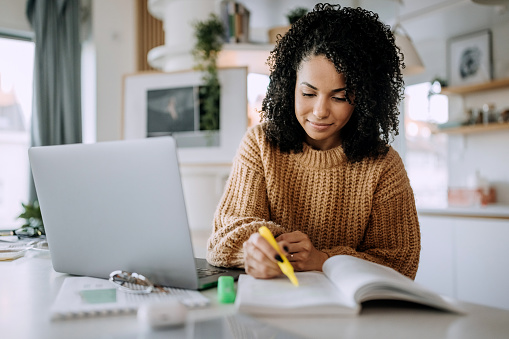 Young beautiful student studying at home, using highlighter