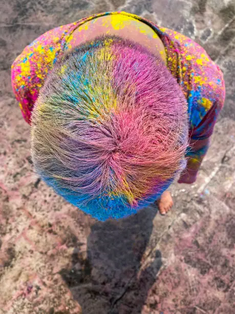 Photo of Image of Hindu Indian man on rooftop covered in paint powder colour, bending over showing hair covered in colourful gulal rang, messing around at Holi festival of colours and love paint fight, elevated view