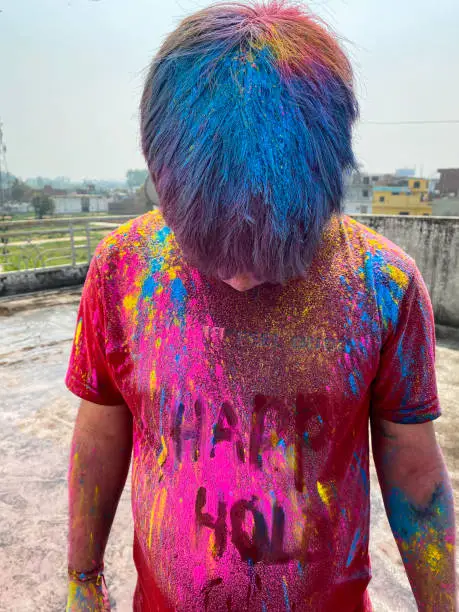 Photo of Image of Hindu Indian man on rooftop covered in paint powder colour, bending over showing hair covered in colourful gulal rang, messing around at Holi festival of colours and love paint fight