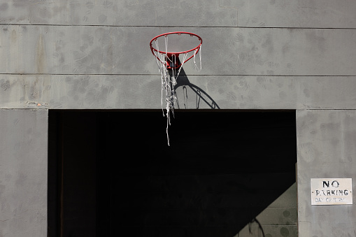 Old red basketball hoop with ragged net attached to a wall above an entry.