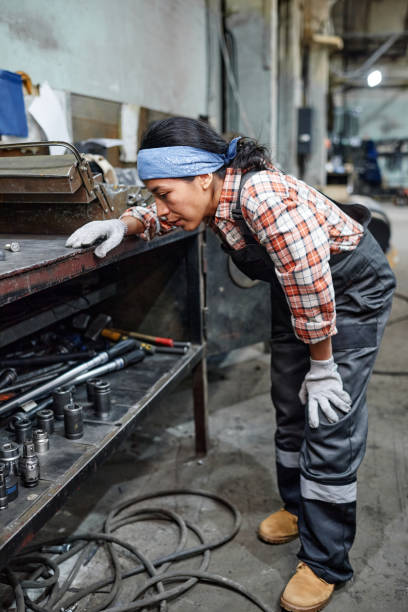 istock Young female technician in workwear bending in front of workbench with tools 1387074451