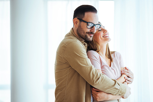 Cheerful young couple looking outside window. Portrait of smiling couple thinking about the future. Happy cheerful couple relaxing at home.