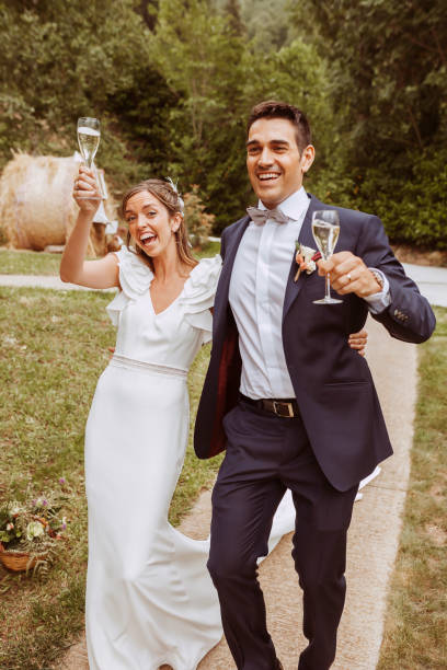 Happy wedding couple walking with glasses of champagne at garden Happy smiling wedding couple walking with glasses of champagne in the hand. Bride and groom. Newlyweds enjoying romantic moment together during wedding day. hands of bride and bridegroom in wedding marriage ceremony stock pictures, royalty-free photos & images