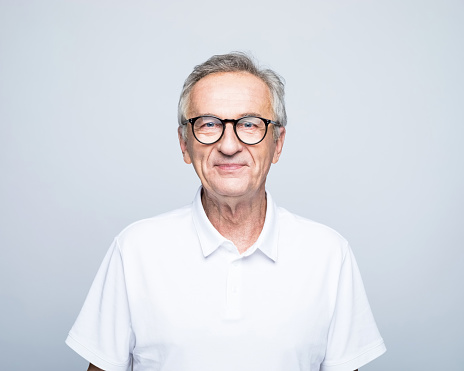 Portrait of smiling retired elderly man wearing eyeglasses standing against gray background