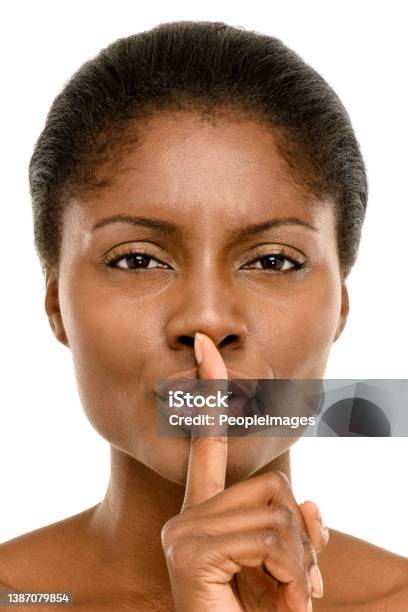 Studio Shot Of A Young Woman Placing Her Finger On Her Lips Against A White Studio Background Stock Photo - Download Image Now