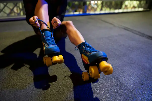 Close-up of an unrecognized Caucasian female sitting on the ground while trying to tie her roller skates.