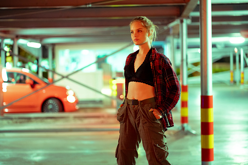 A young Caucasian woman  posing at the parking lot of a public garage, looking at the camera.