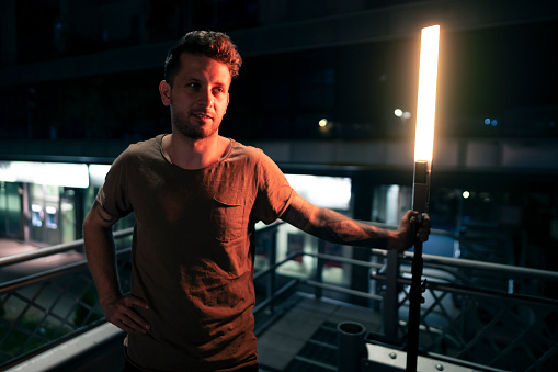 Young, urban Caucasian man standing in a public garage while holding a light stick that glows in dark.