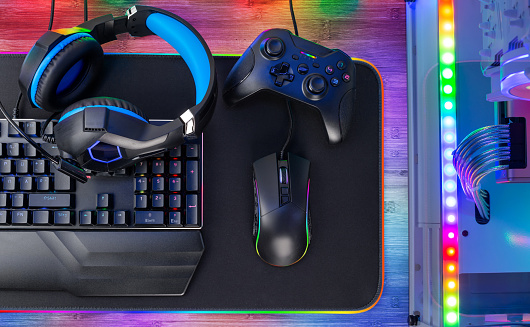 Top view of a colorful bright pc rgb LED gaming desk with headset keyboard mouse and desktop computer.  esports technology concept background
