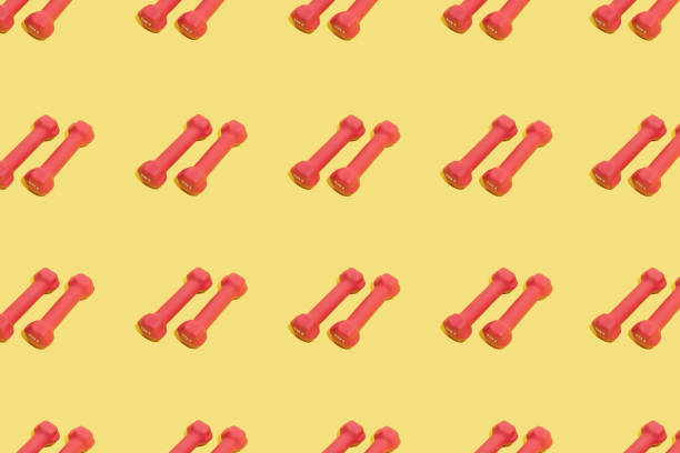 istock Red dumbbells for home workouts on a yellow top view background. Pattern. Equipment for home fitness exercises. Women's accessory for a healthy lifestyle, sports. Sports training with weights. 1387085670