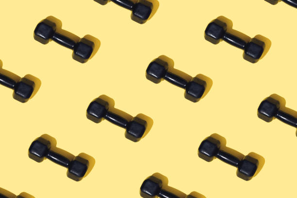 istock Black dumbbells for home workouts on a yellow top view background. Pattern. Equipment for home fitness exercises. Healthy lifestyle, sports. Sports training with weights. 1387085702
