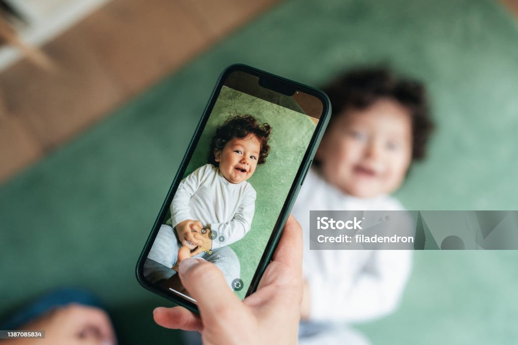 Mother taking photo of her baby Mother taking photos of her baby using smartphone at home. Photographing Stock Photo