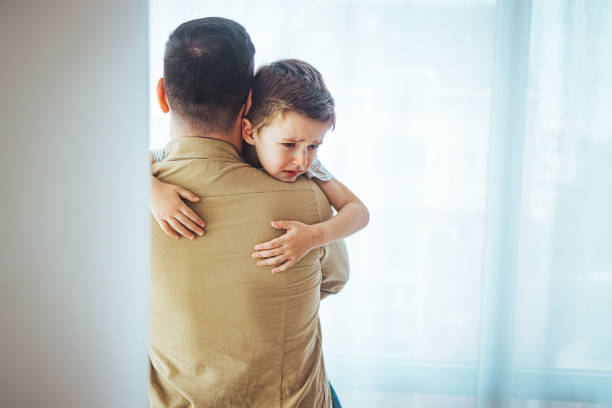 istock Sad young blond boy crying on father hands indoor. 1387086778