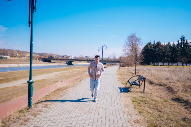 Athletic young man running on a track next to a river while wearing headphones.