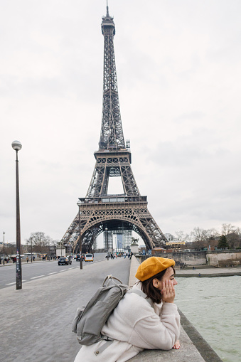 Photo of a young woman exploring Paris during the off-season alone; taking photos from Pont d'Iéna bridge near The Eiffel Tower.