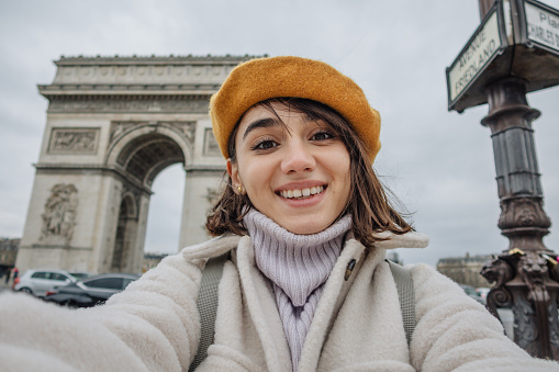 Self-portrait photo of a young woman in front of The Arc de Triomphe; traveling to Paris alone, during the off-season.