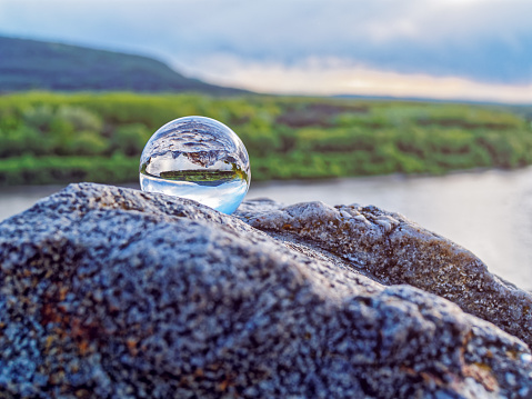 Magic glass ball on old stones. In the background is a river, a spring forest and a cloudy sky