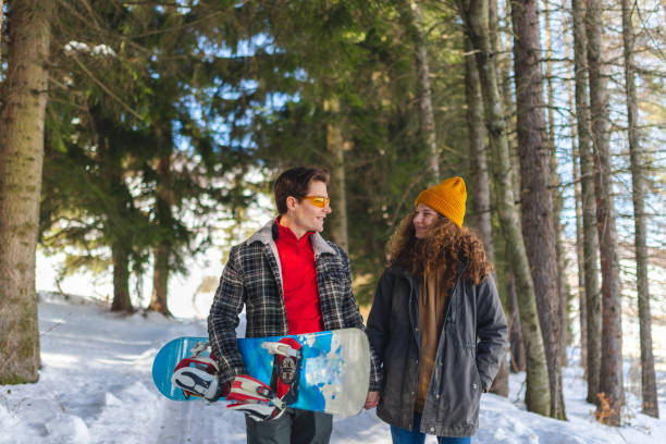 istock Beautiful young heterosexual couple walking on a path in a snowy forest while holding a snowboard 1387096278