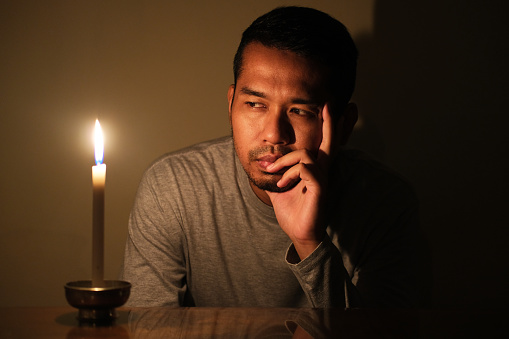 Adult Asian man looking to the burning candle with sad expression during electricity power failure