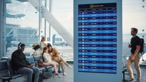 istock Airport Terminal: Young Man Looking at Arrival and Departure Information Display Looking for His Flight. Backgrond: Diverse Crowd of People Wait for their Flights in Boarding Lounge of Airline Hub 1387096736