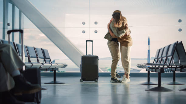 réunion de famille du terminal de l’aéroport: un couple magnifique se rencontre dans la salle d’embarquement. une petite fille souriante rencontre l’amour de sa vie après une longue séparation et des câlins et des danses avec son beau partenaire - salle dembarquement photos et images de collection