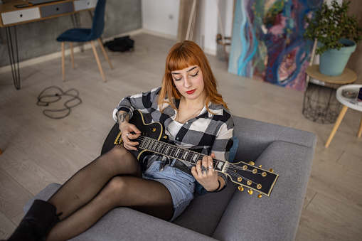Teenage girl playing electric guitar at home