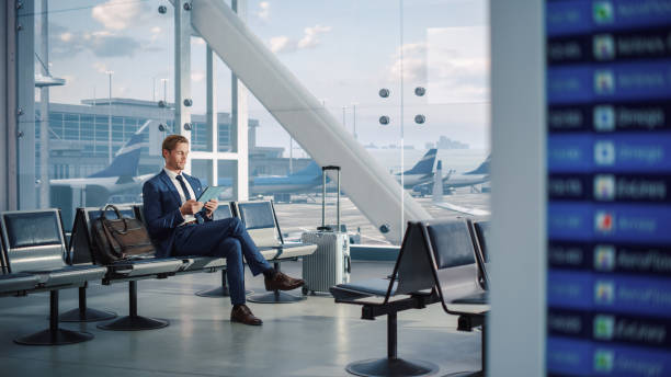 istock Airport Terminal Flight Wait: Businessman Uses Digital Tablet Computer App for e-Business, Browsing Internet. Traveling Entrepreneur Remote Work Online, Sitting in Boarding Lounge of Airline Hub 1387099744