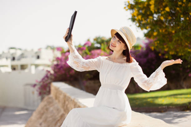 Side view of cheerful business woman sitting using touch screen on tablet pc. Tropical summer outdoors background. Travel lifestyle modern business, selfie photography, online shopping or playing game