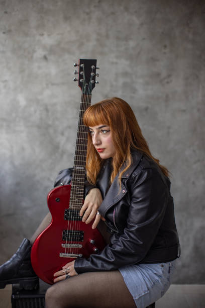 istock Rocker chick sitting on amplifier and holding red electric guitar 1387101375
