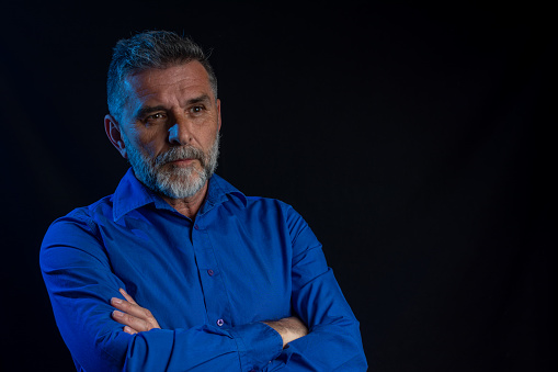 Portrait of an attractive mature bearded man in black studio. Strict male portrait. Dramatic portrait of a man in a low key with blue neon light. low key photo concept.