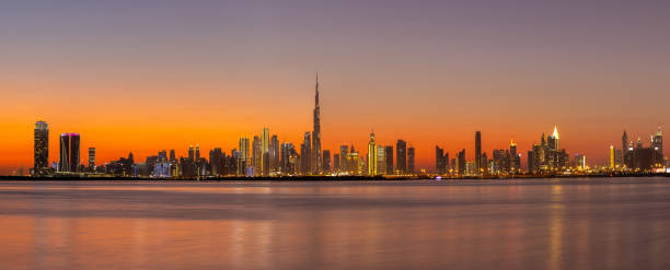 Panorama of Dubai Business Bay skyline at night after sunset with colorful illuminated buildings and calm Dubai Creek water. Panorama of Dubai Business Bay skyline at night after sunset with colorful illuminated buildings and calm Dubai Creek water. dubai skyline stock pictures, royalty-free photos & images