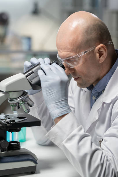 istock Side view of bald mature man in whitecoat using microscope 1387108176