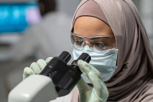 Primer plano de una joven investigadora musulmana mirando en el microscopio photo