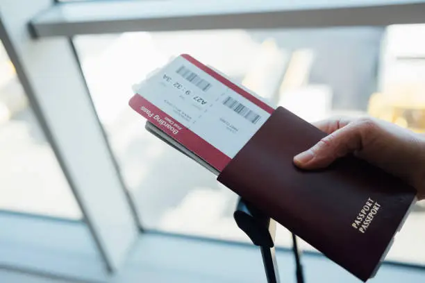 A close up shot of an anonymous person holding his passport, ticket and other documents necessary for going abroad.